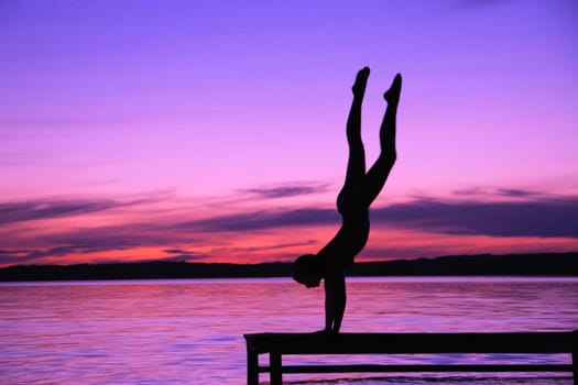 A person in a hand stand on a dock against a sunset
