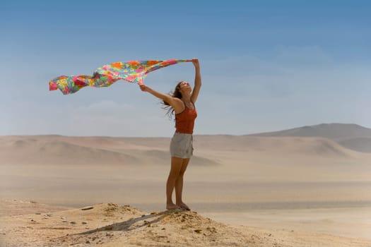 A woman holds up a scarf to the desert wind