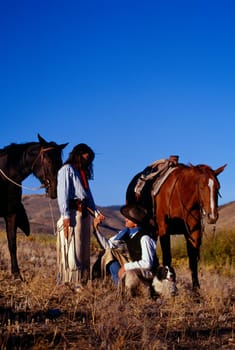 Cowboy and cowgirl holding hands beside their resting horses, Ponderosa Ranch.