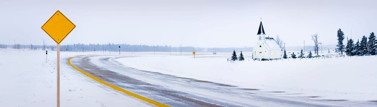 Old fashioned steeple church with road in winter