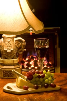 Cheese, grapes and glass of wine on table by lamp