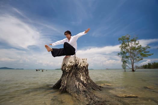 A man balancing on a tree stump on a beach in Koh Lanta,Thailand