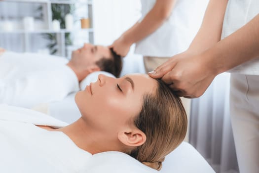 Caucasian couple enjoying relaxing anti-stress head massage and pampering facial beauty skin recreation leisure in dayspa modern light ambient at luxury resort or hotel spa salon. Quiescent