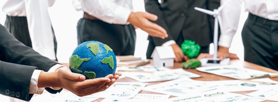 Businessman hand holding paper Earth with business people on meeting in office, planning and implementing eco-friendly ideal for corporate policy to reduce CO2 emission and save earth. Trailblazing