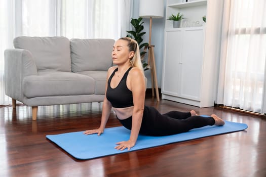 Senior woman in sportswear being doing yoga in meditation posture on exercising mat at home. Healthy senior pensioner lifestyle with peaceful mind and serenity. Clout