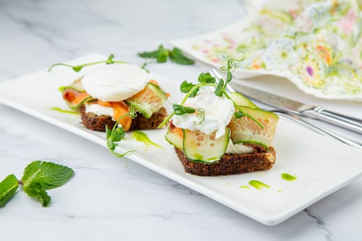 canapes on black bread with cheese, red fish, herbs and cucumber