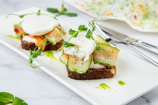 canapes on black bread with cheese, red fish, herbs and cucumber