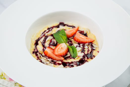 porridge with strawberries, mint and berry jam in a white plate