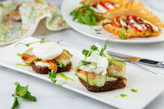 canapes on black bread with cheese, red fish, herbs and cucumber