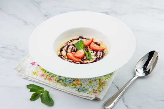 porridge with strawberries, mint and berry jam in a white plate