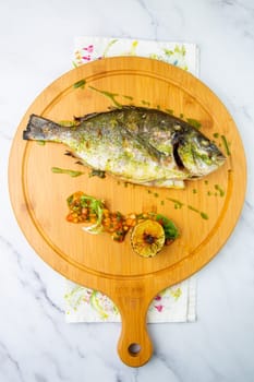 baked fish with spices and lemon on a wooden tray