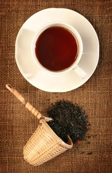 A wicker scoop with herb tea leaves and a cup of tea