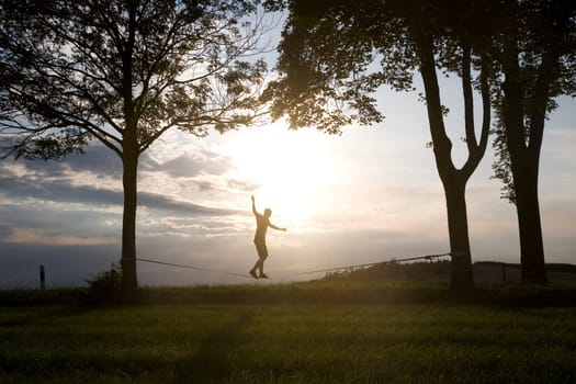 young man on the slackline in sunset