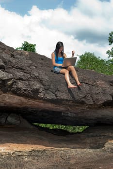 Teenage boy with laptop sitting on rocks