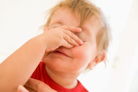 Baby indoors putting hand over face