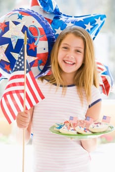 Young girl outdoors on fourth of July with flag and cookies smiling