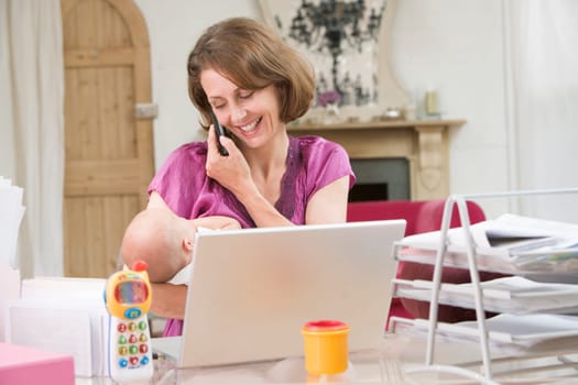 Mother and baby in home office with laptop and telephone
