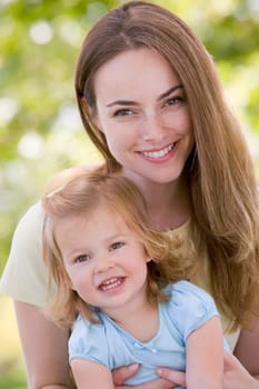 Mother holding daughter outdoors smiling