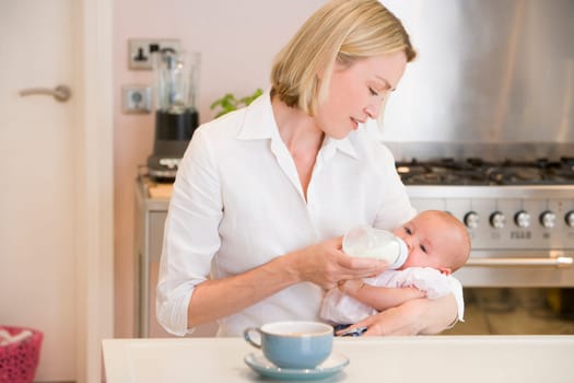 Mother feeding baby in kitchen with coffee