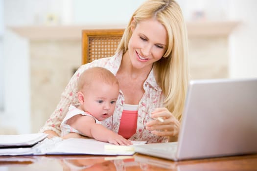 Mother and baby in dining room with laptop smiling