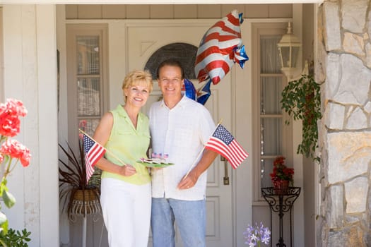 Couple at front door on fourth of July with flags and cookies smiling