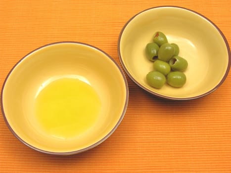 Two ceramic bowls with olive oil and olives on orange background