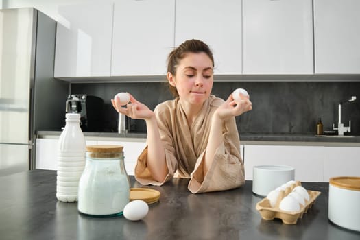 Attractive young cheerful girl baking at the kitchen, making dough, holding recipe book, having ideas.