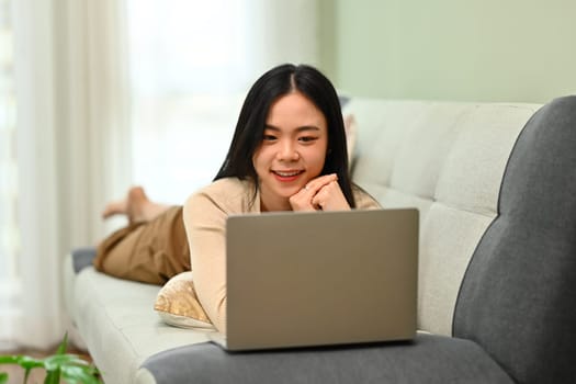 Carefree young woman lying on couch at using laptop. Technology and lifestyle concept.