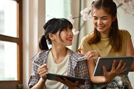 Two smiling creative women holding digital tablets sharing ideas, discussing ideas and brainstorming at office.