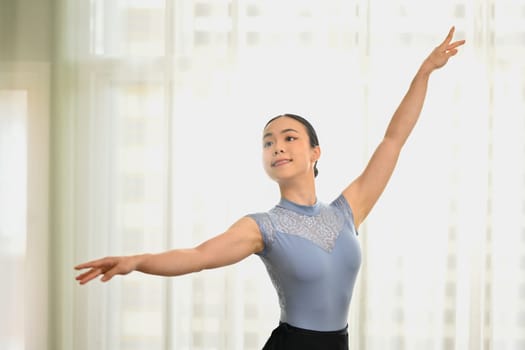 Beautiful ballerina dancing with graceful hands near window in studio. Dance, art and education concept.