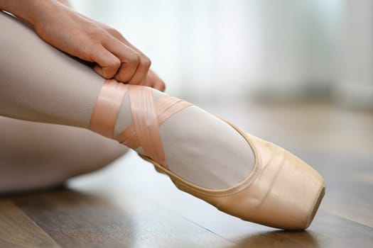 Close up ballerina tying pointe shoes in dance studio. Art, dance, people and inspiration concept.