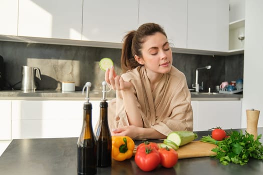 Portrait of brunette woman, wife cooking at home, making dinner, posing near chopping board in kitchen with vegetables, holding zucchini.