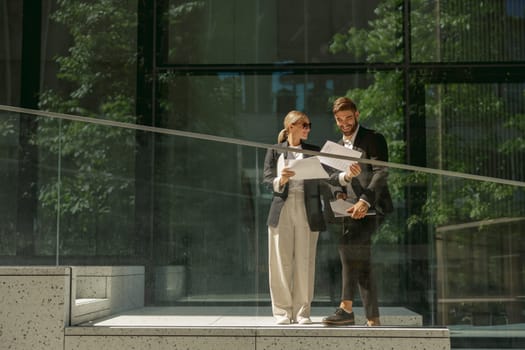 Business colleagues working with documents while standing on background of modern office building