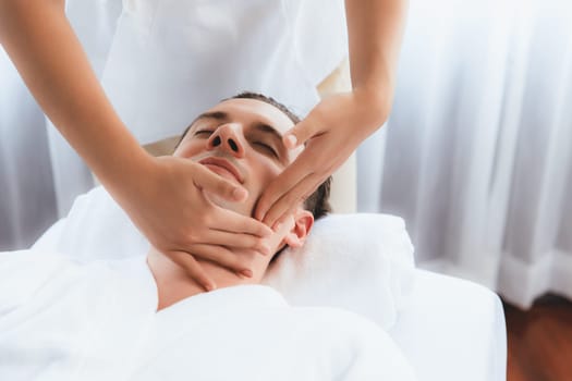 Caucasian man enjoying relaxing anti-stress head massage and pampering facial beauty skin recreation leisure in dayspa modern light ambient at luxury resort or hotel spa salon. Quiescent