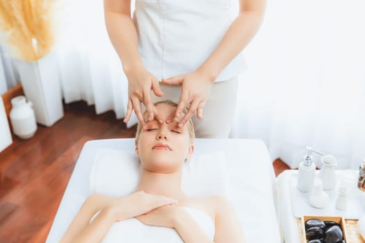 Caucasian woman enjoying relaxing anti-stress head massage and pampering facial beauty skin recreation leisure in dayspa modern light ambient at luxury resort or hotel spa salon. Quiescent