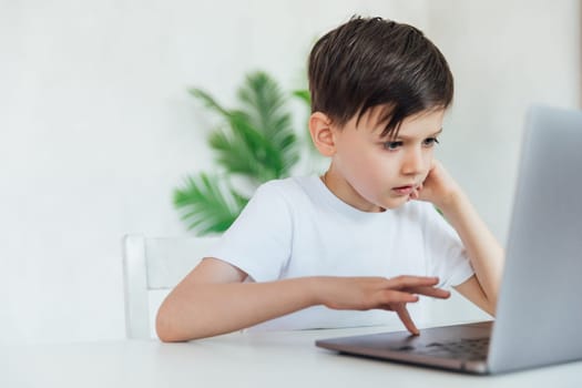 child sits with a laptop at a table in a room with a green plant