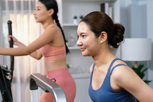 Energetic and strong athletic asian woman running on elliptical running machine at home with workout buddy or trainer. Pursuit of fit physique and commitment to healthy lifestyle. Vigorous