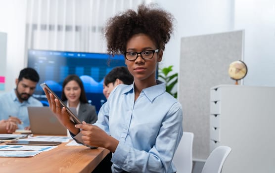 Happy young african businesswoman wearing glasses portrait with group of office worker on meeting with screen display business dashboard in background. Confident office lady at team meeting. Concord