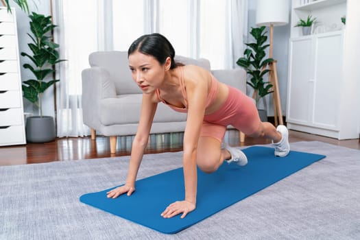 Asian woman in sportswear doing burpee on exercising mat as home workout training routine. Attractive girl engage in her pursuit of healthy lifestyle and fit body physique. Vigorous