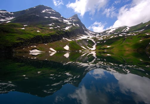 Reflection of peaks,snow and clouds in a mountain lake