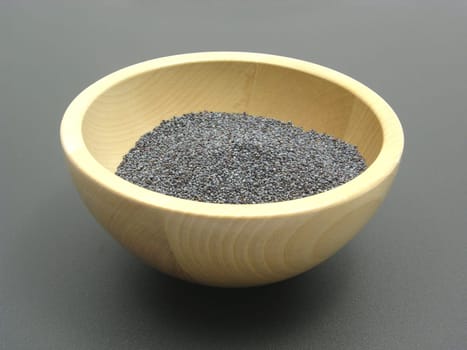 Wooden bowl with poppy seeds on a matt base