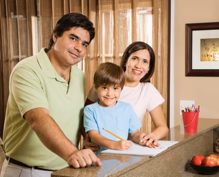 Hispanic parents and son with homework smiling at viewer.
