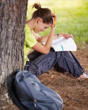 young woman studying outdoors and leaning on tree