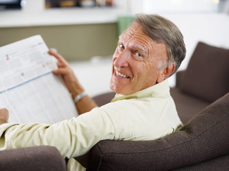 senior man reading newspaper at home and looking over shoulders