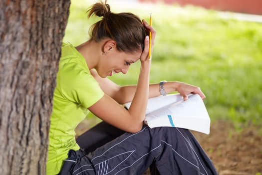 young woman studying outdoors and leaning on tree
