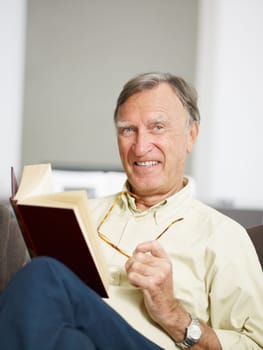 senior man reading book at home and looking at camera. Copy space
