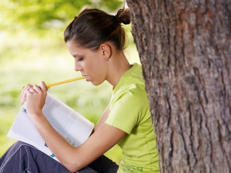 young woman studying outdoors and leaning on tree. Copy space