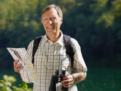 senior hiker holding map and binoculars and looking at camera. Copy space