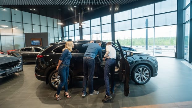 The seller demonstrates the interior of the car to buyers. Caucasian couple chooses a car