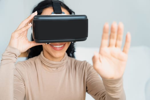 Young woman using virtual reality VR goggle at home for crucial online shopping experience. The virtual reality VR innovation optimized for female digital entertainment lifestyle.